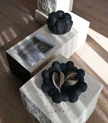Taiteellisia mustia keramiikkakulhoja esillä minimalistisilla kivipöydillä luonnollisin pintatekstuurein