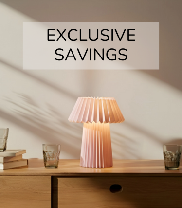 Vaaleanpunainen pöytävalaisin puisella lipastolla, jota ympäröivät lasit ja kirjat lämpimässä auringonvalossa.